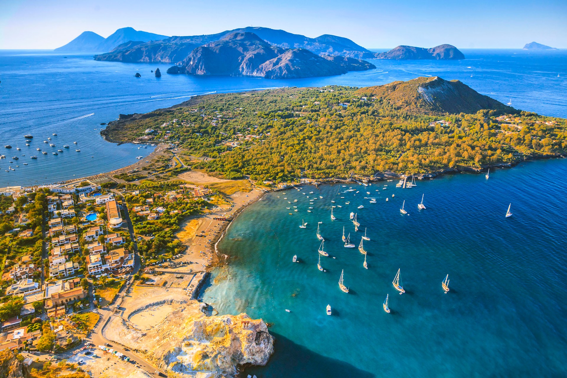 vista aerea di vulcano, con la pozza dei fanghi e le acque calde, la spiaggia di levante, il vulcanello e le barche, sullo sfondo lipari, salina e panarea.