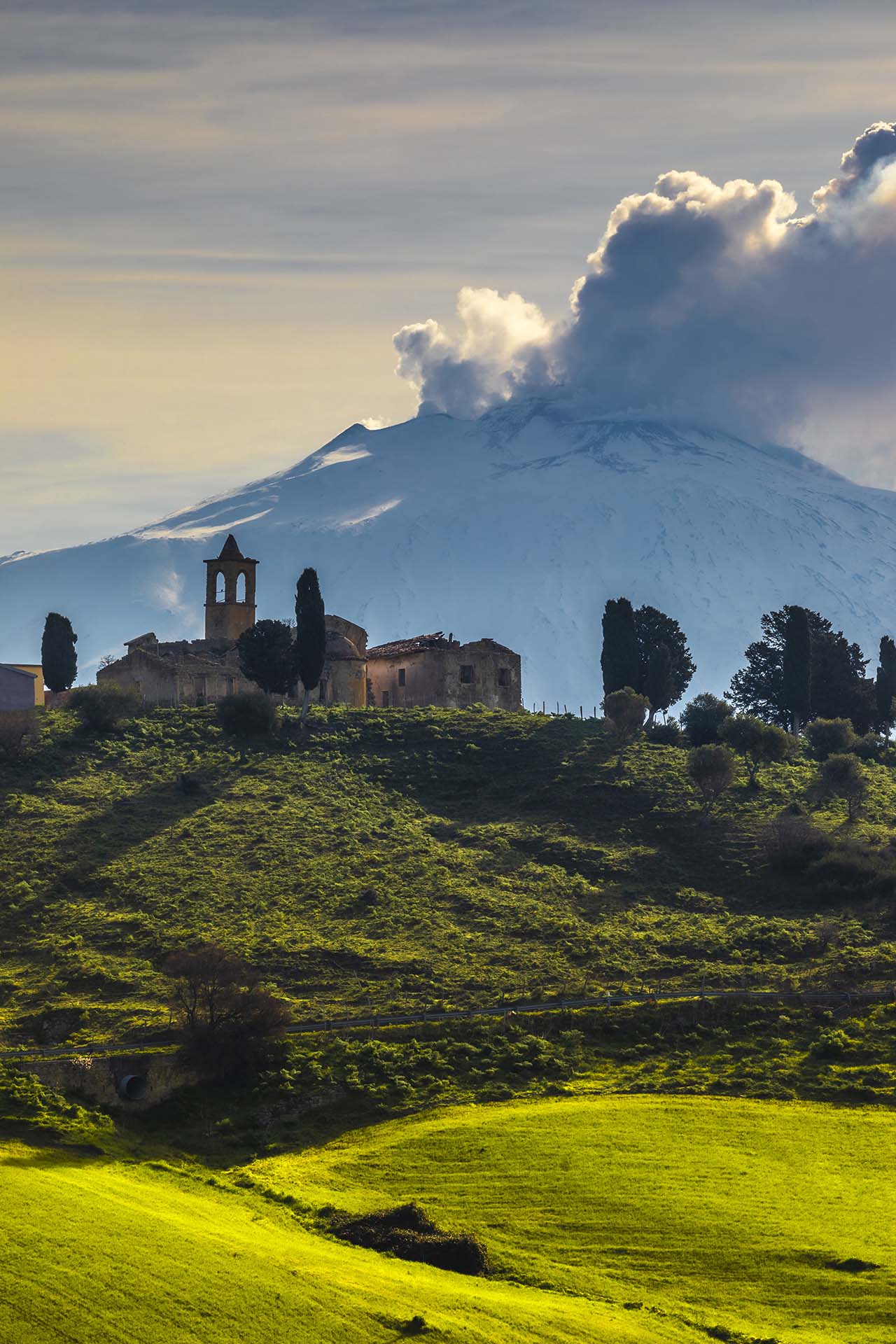 Borgo Giuliano tra prati verdi e l'Etna vestita di bianco in attività vulcanica