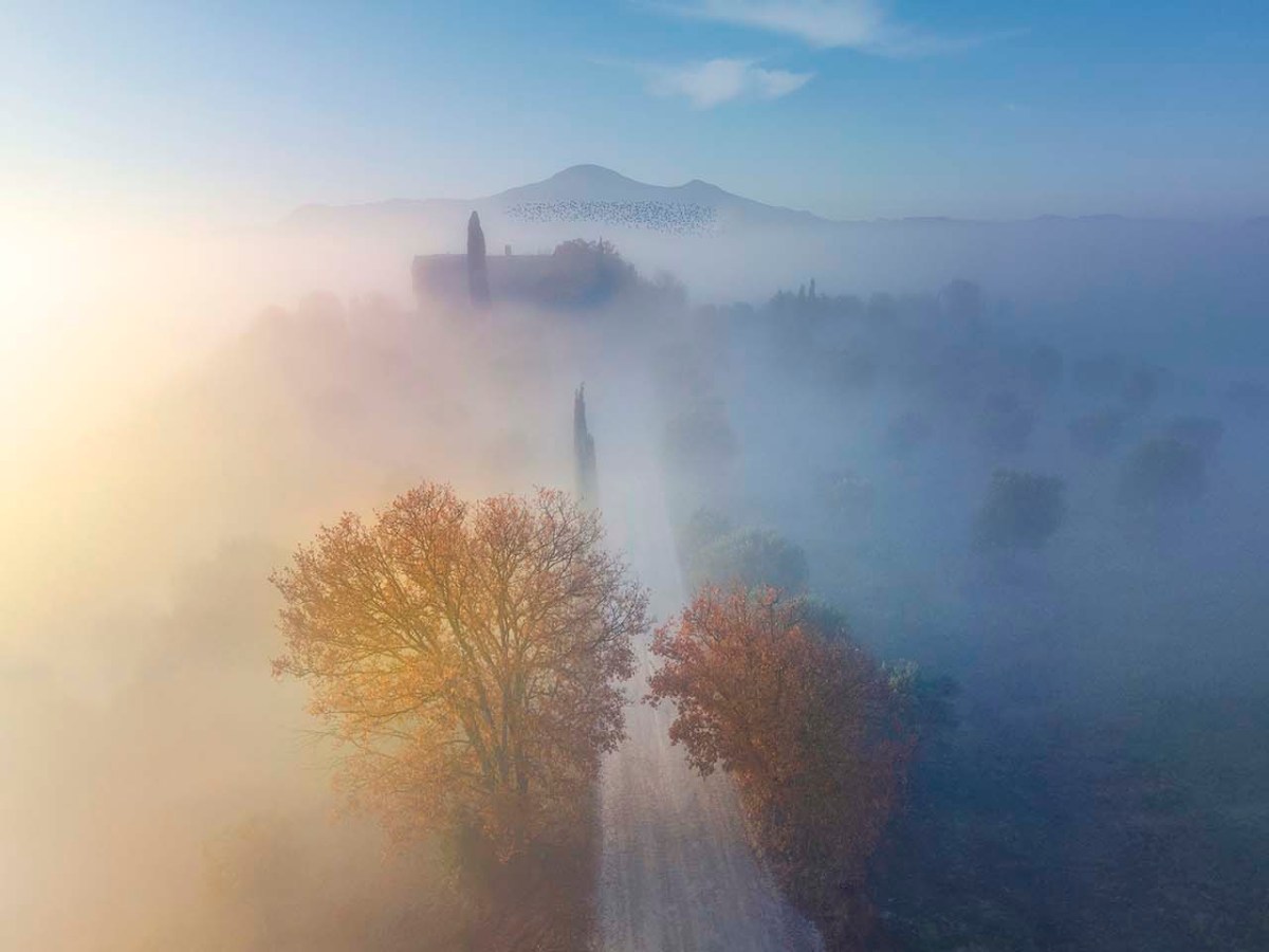 Strada nella nebbia tra le colline della Val d'Orcia con il Monte Amiata.