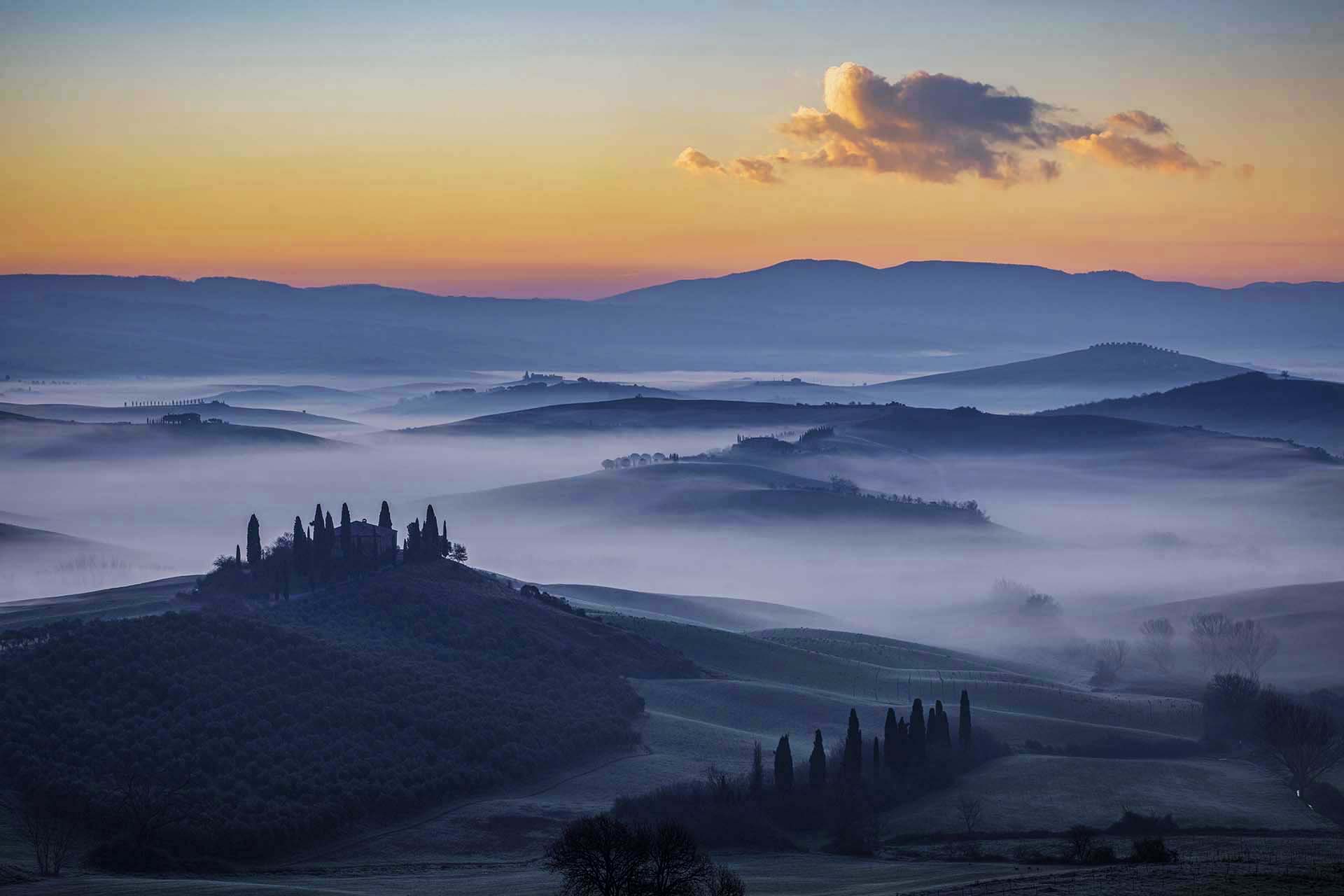 Paesaggio collinare della Val d’Orcia nella Toscana senese avvolto dalla nebbia mattutina.
