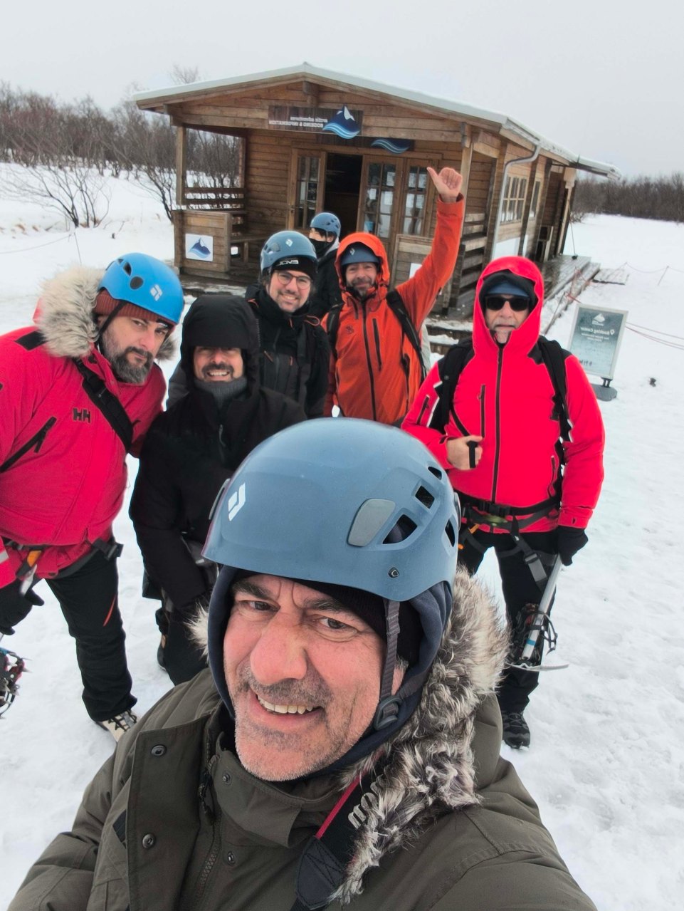 Escursionisti con caschi e abbigliamento invernale davanti a rifugio ghiacciato.
