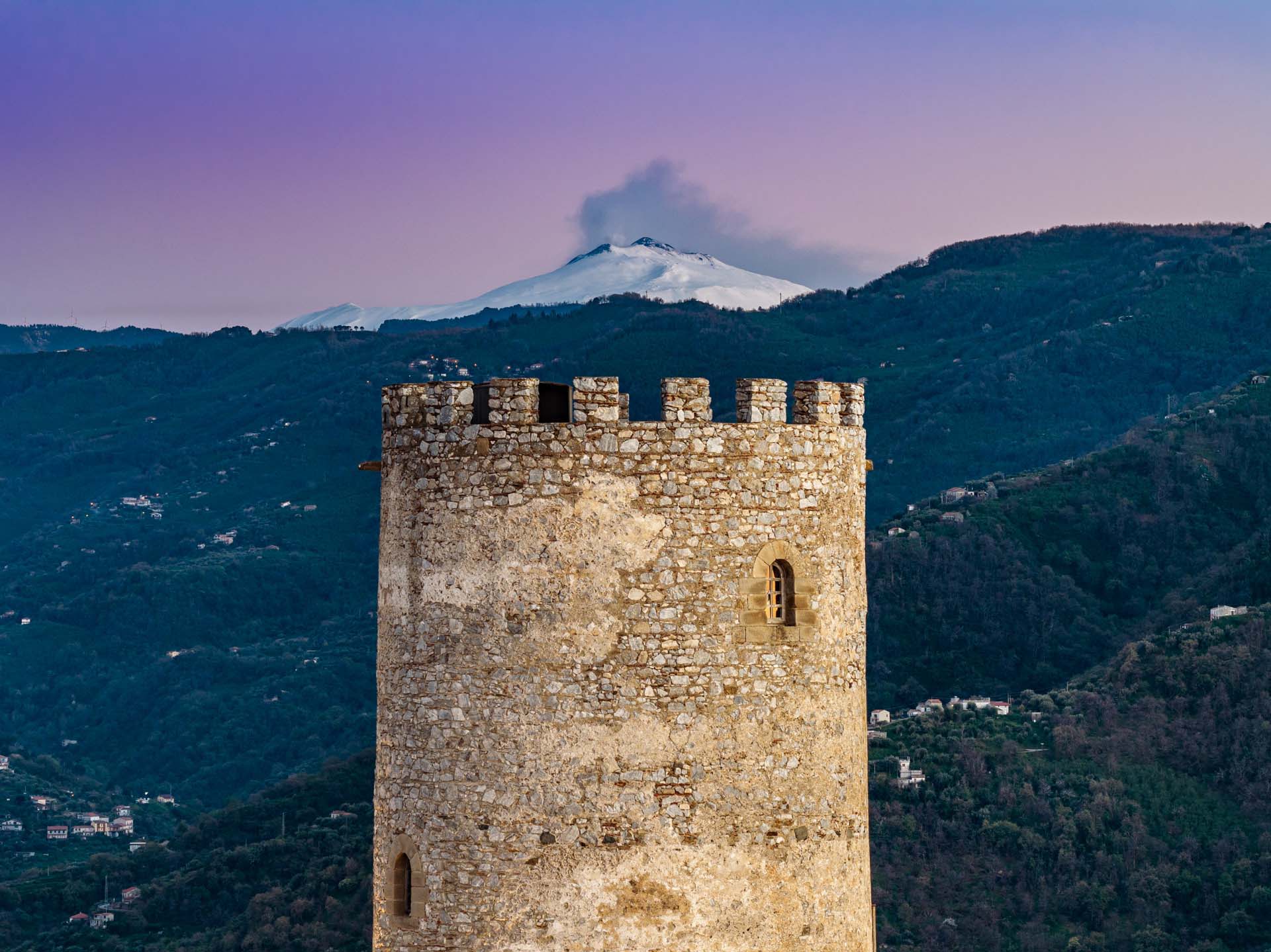La Torre Saracena di Piraino in primo piano con l'Etna innevato sullo sfondo al crepuscolo