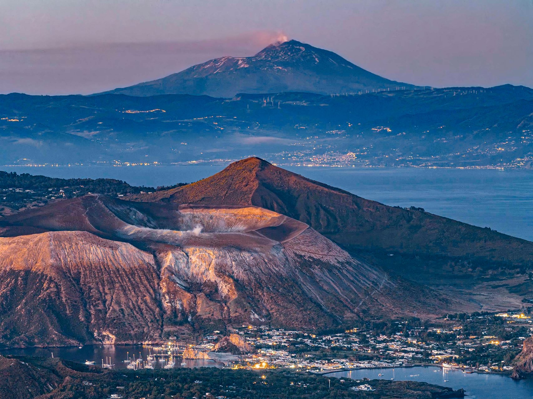 Cratere dell'isola di Vulcano con fumi sulfurei e il Monte Etna sullo sfondo della costa siciliana