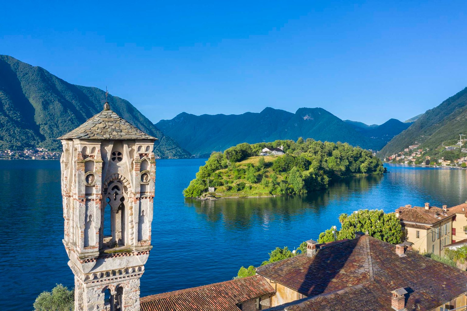 Il campanile romanico della Chiesa di Santa Maria Maddalena a Ossuccio, che si affaccia sulle acque del Lago di Como con la vicina Isola Comacina sullo sfondo.