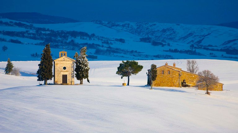 Paesaggio toscano in inverno, con la neve che copre le colline e la celebre Cappella di Vitaleta.