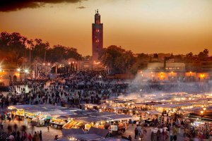 Piazza Jemaa el-Fnaa a Marrakech, in Marocco, al tramonto, con le sue caratteristiche bancarelle illuminate e il minareto della moschea della Koutoubia sullo sfondo