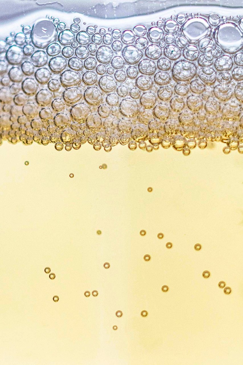 Primo piano ravvicinato delle bollicine (perlage) e della schiuma superficiale di un champagne
