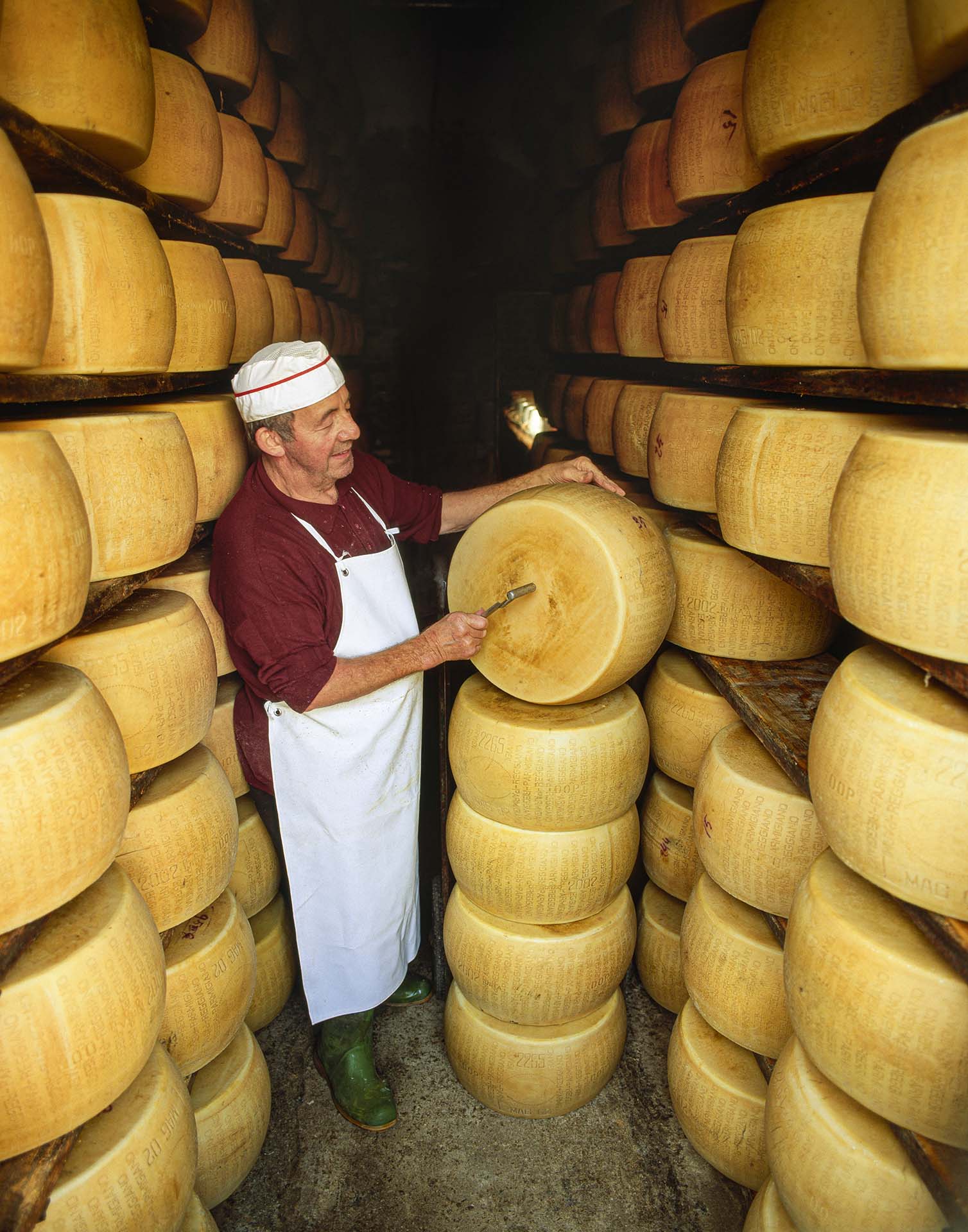 Magazzino di stagionatura di Parmigiano Reggiano dove il casaro esamina una forma di formaggio con il tradizionale martelletto